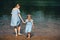 Young woman and her daughter barefoot walk in the water on a river. Back view