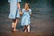 Young woman and her daughter barefoot walk in the water on a river. Back view. Closeup