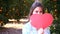 Young woman hiding behind red paper heart