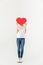 young woman hiding face behind red heart symbol