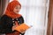 Young woman hijab holding and looks a book standing near windows