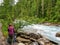 A young woman hiker setting up her campsite at a remote campground along a beautiful river surrounded by green evergreen forest