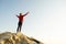 Young woman hiker standing alone on big stone in mountains. Female tourist raising her hands up on high rock in morning nature.