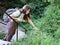 Young woman hiking with backpack standing on steps on forest path and collects wildflowers