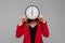 Young woman Holding Big Clock Covering her Face, she wonders how much time passed, standing in red blazer against gray background