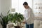 Young woman holding can watering houseplant in living room