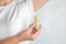 Young woman holding  crystal alum deodorant near armpit on light blue background, closeup