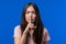 Young woman holding finger on lips, blue studio background. Pretty teen girl with gesture of shhh, secret, silence