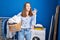 Young woman holding laundry basket doing ok sign with fingers, smiling friendly gesturing excellent symbol