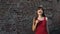 Young woman holding a mustache on a stick, standing next to a brick wall.