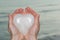 Young woman holding polished cream white carved Onyx Heart in her hands at the sunrise in front of the lake. Love, Romance