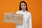 Young woman holding sign with word Unemployed on orange background
