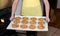 Young woman holding tray of oatmeal cranberry cookies fresh out of oven, cat in background