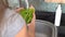 Young woman holds a bunch of spinach under running water, preparing it for cooking, rear view