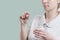 Young woman holds pill and glass of clean water isolated on pistachio background. Health concept. Drug treatment. Take pills.