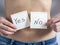 A young woman holds two paper stickers in front of her bare stomach. The stickers say Yes and No. The concept of a possible