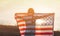 A young woman holds the US national flag in a field at sunset. 4th of July, Independence day. American freedom concept