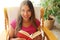 Young woman at home sitting on comfortable chair relaxing in her living room reading book. Looks at camera