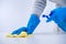 Young woman housekeeper in apron is cleaning, wiping down table surface with blue gloves