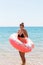 Young woman with inflatable ring cold shivering sad crossed arms black bikini swimsuit standing in sea water. Summer holidays and