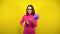 A young woman inflates a purple balloon with a pump on a yellow background. Girl in a pink turtleneck and glasses.
