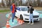 Young woman with instructor near car and fallen traffic cone outdoors. Failed driving school exam