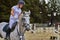 Young woman jockey in white dress and black boots  takes part in equestrian competitions.