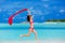 Young woman jumping on the beach with a red scarf