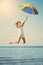 Young woman jumping with rainbow umbrella on the beach. Scene of