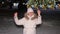 A young woman jumps and has fun near the Christmas tree in the open air, it snows.