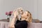 Young woman kisses Yorkshire terrier dog, in her living room on pink sofa. They are happy together. Owner and pet have same color