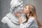 Young woman kissing God Apollo bust sculpture. Ancient Greek god of Sun and Poetry Plaster copy of a marble statue on