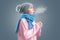 Young woman in a knitted hat and blue scarf is trying to keep warm, breathing. Gray background. The concept of energy