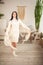 Young woman in a knitted white dress sweater with a knitted retro shawl. Girl in vintage romantic interior is dancing with a hand-