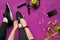 Young woman laces sneakers, preparing for training. Bottle of water, yoga mat, phone, headphones on purple background