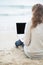 Young woman with laptop on cold beach. rear view