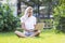 Young woman with laptop sits on the grass in a summer park. Blonde with long hair in a white tank top and shorts. Sunny day.