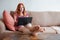 young woman with laptop working from home sitting on sofa with feet on table