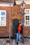 Young woman leaning against a lamppost in front of a house with a very narrow door