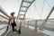 A young woman is leaning on the bridge fence while typing on her phone. An electric scooter is parked next to her