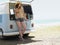 Young woman leaning on open tailgate of camper van parked by sea