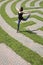 Young Woman Leaping Over a Grass Maze