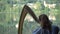 Young woman learns to play musical instrument in nature near pond. Private lesson on pier by lake in playing harp in
