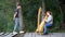 Young woman learns to play musical instrument in nature near pond. Private lesson on pier by lake in playing harp in