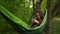 A young woman lies in a hammock in the woods with a phone in her hands. A girl with glasses chats on the Internet