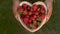 Young woman lifting a heart shaped wooden bowl of fresh red strawberries to camera