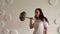 Young woman lifts multicolored barbell against white patterned wall. Adult lady doing sport, using all her strength