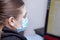 Young woman in light blue medical sterile mask works on comptuter.