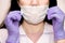 A young woman in lilac medical gloves puts a protective mask on her face . A confident girl, a female doctor in a