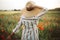 Young woman in linen dress and hat enjoying rural evening among poppy and cornflowers in countryside. Stylish girl in rustic dress